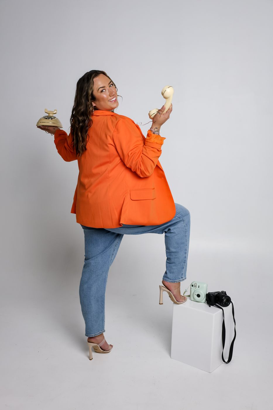 Zoe in an orange blazer holding a cream rotary phone on white