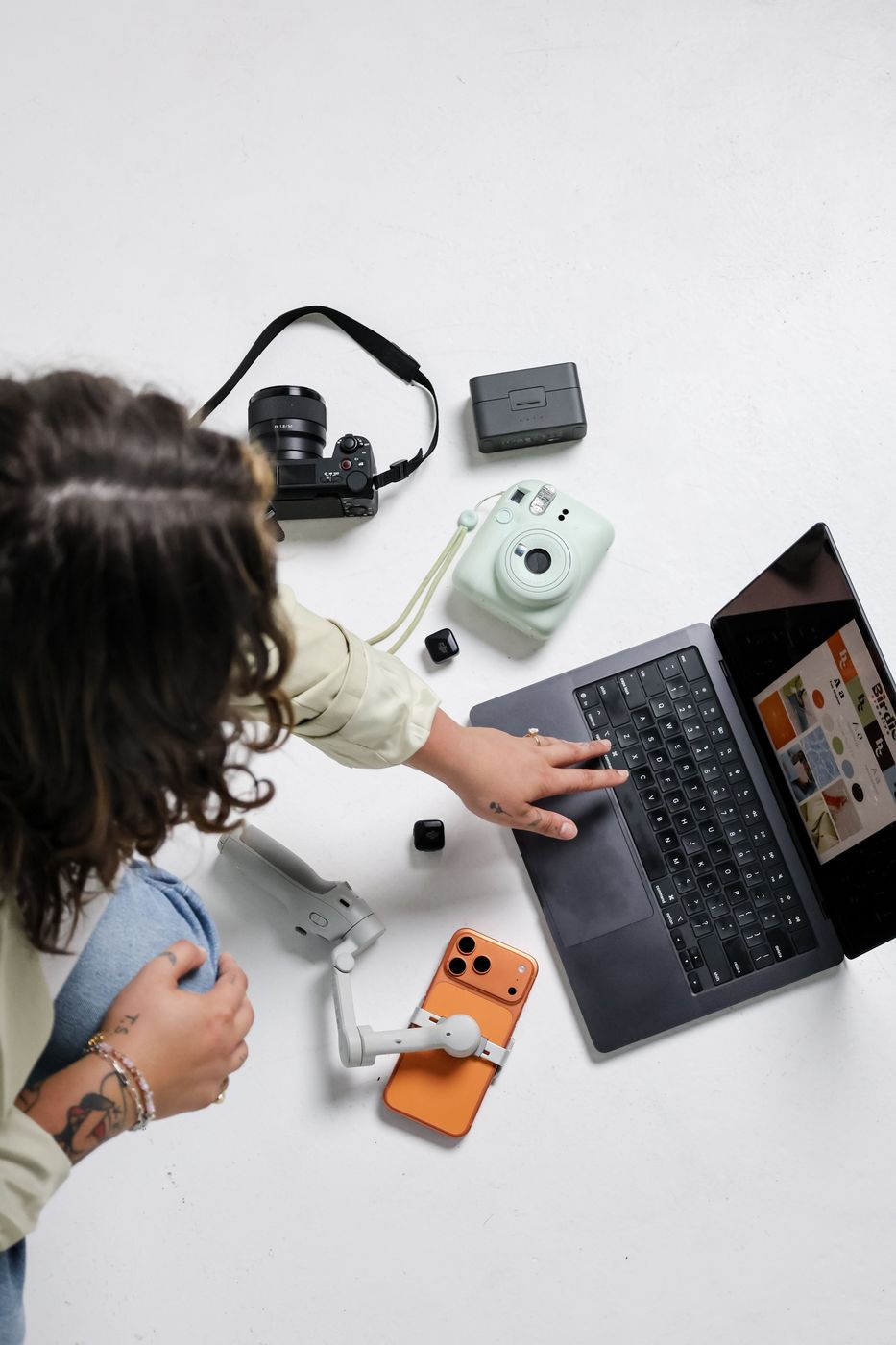 Overhead flat lay of cameras, gimbal, phone and laptop on white