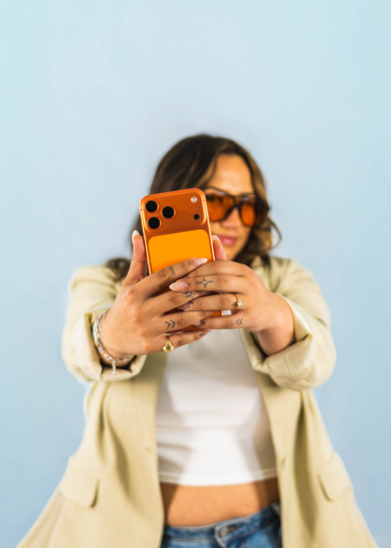 Zoe Kasper holding an orange phone in front of a sky blue backdrop