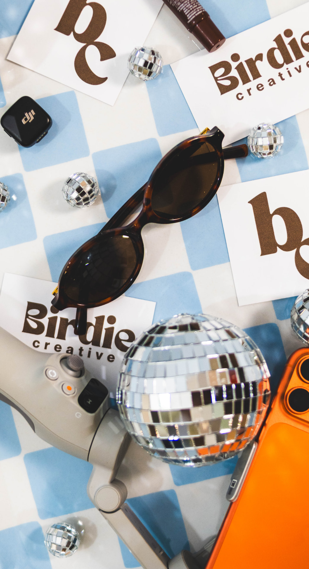 Birdie Creative brand cards, camera equipment, sunglasses and disco balls on a blue checkerboard
